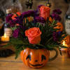 Orange roses and purple flowers arranged in a pumpkin mug