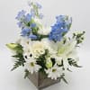 White daisies and lilies with blue delphinium in a wooden box