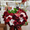Red roses and white orchids arranged in a round box with butterfly picks