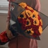 Person holding a bouquet of red roses and yellow flowers wrapped in black paper