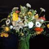 Tall mixed bouquet in a green glass vase with yellow, white, and orange flowers