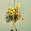 Tall yellow orchid arrangement in a clear glass vase with orange blooms