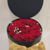 Black round gift box filled with red roses and a gold bow