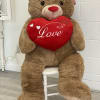Large teddy bear holding a red heart pillow with the word Love