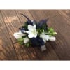White floral corsage with dark blue ribbon accents on a wooden surface