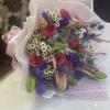 Bouquet of pink roses, lilies, and purple flowers wrapped in white paper