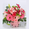 Pink lilies, roses, and gerbera daisies in a glass cube vase with pink ribbon and butterfly accents