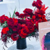 Red rose arrangement in a black vase with tropical foliage accents