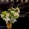 Tall floral arrangement with white and green blooms in a glass vase