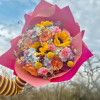 Colorful bouquet with sunflowers, roses, and small daisies wrapped in bright pink paper