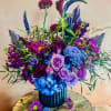 Purple and blue floral arrangement in a dark vase