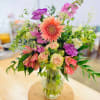 Mixed bouquet of pink, peach, and purple flowers in a clear glass vase