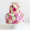 Tiered floral cake with pink and white roses topped by a gold crown