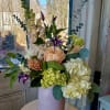 Mixed bouquet in a pale pink vase with peach, white, and purple flowers