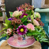 Pink and purple flower arrangement in a floral teacup and saucer