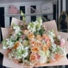 Bouquet of peach and white roses with white filler flowers in pink wrapping
