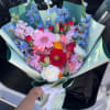 Colorful mixed bouquet with gerbera daisies, tulips, and blue flowers wrapped in mint paper