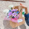 Bouquet of white and purple flowers in a kraft gift bag with a drink cup