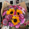 Bouquet of yellow sunflowers, pink roses, and purple flowers wrapped in brown paper
