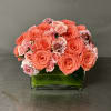 Coral and pink roses arranged in a square glass vase