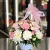 Pink and white flowers arranged in a white basket with a pink ribbon