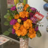 Bright orange and purple flower arrangement in a patterned vase with a skull decoration.