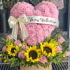 Pink heart-shaped floral arrangement with a Valentine ribbon and sunflowers below