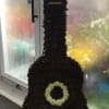 Large guitar-shaped floral arrangement made of dark flowers with pale accents.