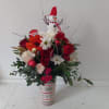 Christmas bouquet with red and white flowers in a patterned vase topped by a snowman ornament