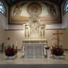 Two red floral arrangements flank a church altar with statues and a crucifix.
