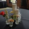 Small floral arrangements in glass vases around tall pillar candles on a table