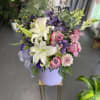 Bouquet of white lilies, pink roses, and purple flowers in a lavender hatbox