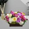 Mixed pink, white, and yellow flowers in a rectangular box with a reed diffuser
