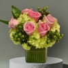Pink roses arranged with pale green hydrangeas in a clear square vase