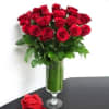 Red roses arranged in a tall glass vase with greenery