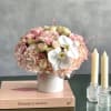 Pink floral arrangement in a white vase beside two candles