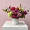 Mixed bouquet of pink, purple, and green flowers in a white vase