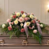 Pastel rose arrangement on a casket with pink ribbon and greenery