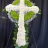 White and green floral cross on a stand against a dark backdrop