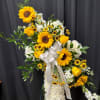 Standing floral spray with sunflowers, white blooms, and a white ribbon