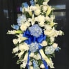 Standing floral spray with white lilies, roses, and blue hydrangeas on a black backdrop
