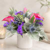Pink calla lilies and purple thistle in a white vase