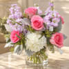Pink roses and lavender flowers arranged in a clear glass vase