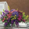 Colorful floral arrangement on a white casket with purple, pink, and blue blooms.