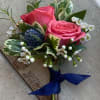 Pink rose boutonniere with white filler flowers and a blue ribbon
