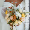 Bride holding a bouquet of cream, yellow, and orange flowers