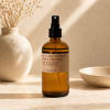 Amber room spray bottle with black pump on a neutral tabletop