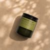 Black jar candle with a green label on a beige surface