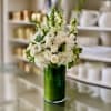 White roses and ranunculus in a tall green glass vase