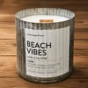 A beach vibes candle in a rustic metal container on a wooden surface